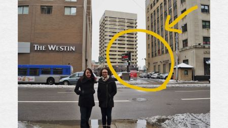 Barbara Hilden and Rebecca Jade stand on 100 St. Behind them is a parking lot between two large buildings (The Westin and the World Trade Centre)