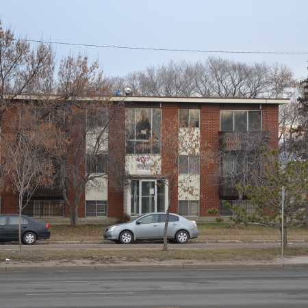 A two and a half story apartment building viewed from across the street, with bare trees all around and a clear blue sky.