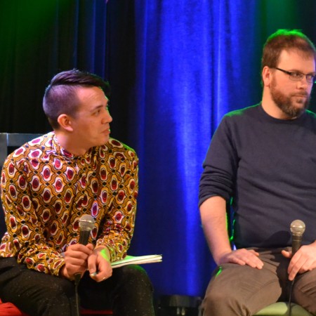Chris and Dan sit with microphones on stage