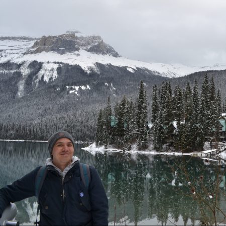 chris stands in front of emerald lake, in winter.